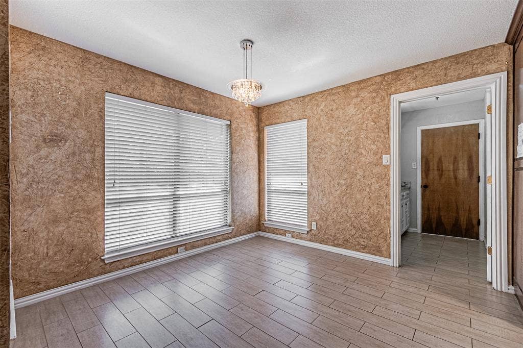 8808 Sylvan Court, Fort Worth, TX 76120 Wood-finish flooring with a crystal chandelier, textured wall finish, and white window blinds