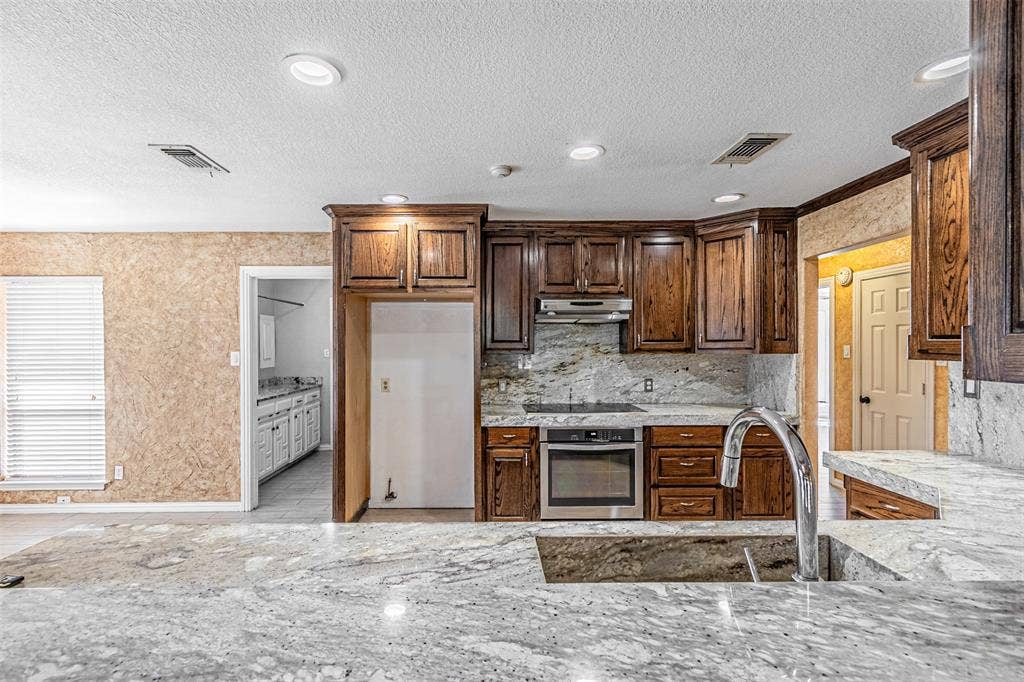 8808 Sylvan Court, Fort Worth, TX 76120 Kitchen featuring extensive cabinetry, stone countertops, a large single-basin sink with a high-arc faucet, and stainless steel appliances including a built-in oven and cooktop