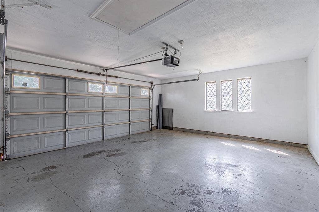 8808 Sylvan Court, Fort Worth, TX 76120 Attached two-car garage featuring a panel door with transom windows, three diamond-paned windows, and a concrete floor
