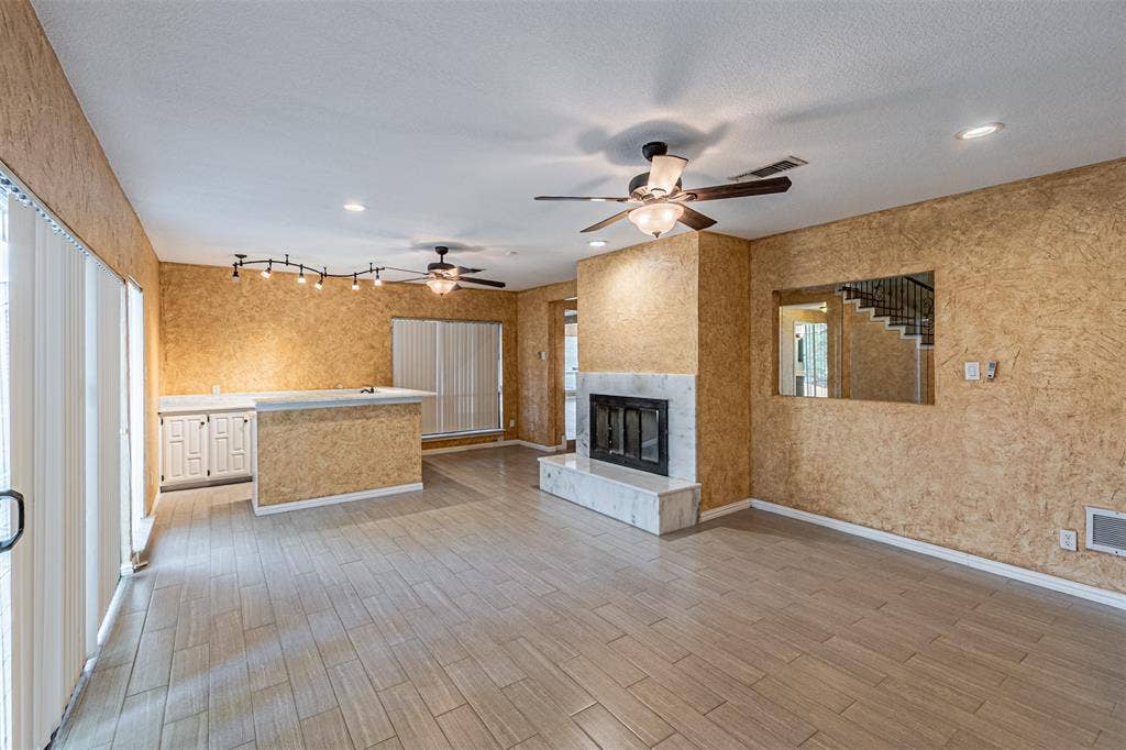 8808 Sylvan Court, Fort Worth, TX 76120 Tile flooring, stone-surround fireplace, built-in cabinetry with light-toned countertop, track lighting, and ceiling fans