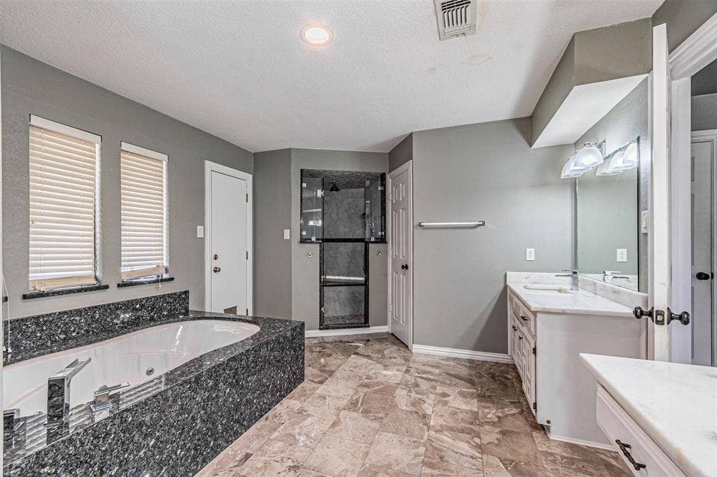 8808 Sylvan Court, Fort Worth, TX 76120 Soaking tub with a dark stone surround, walk-in shower with a glass enclosure, dual vanity with white countertops, and tiled flooring