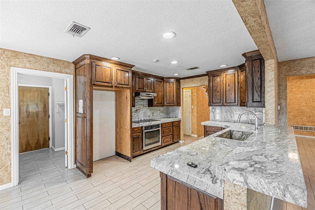 8808 Sylvan Court, Fort Worth, TX 76120 Kitchen featuring wood cabinetry, light-toned stone countertops, a stainless steel sink with a gooseneck faucet, an integrated cooktop, and light-toned tile flooring