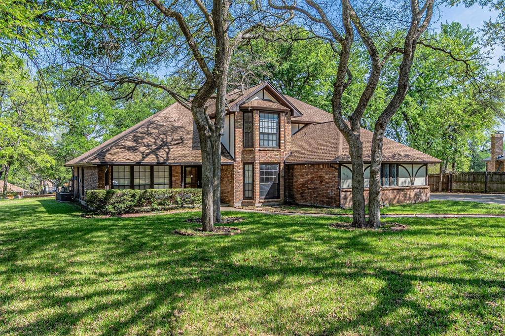 8808 Sylvan Court, Fort Worth, TX 76120 Brick exterior residence with a shingled roof, mature trees, and a manicured lawn