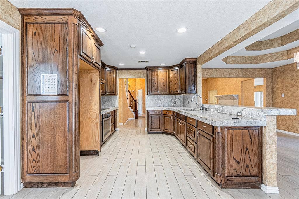 8808 Sylvan Court, Fort Worth, TX 76120 Wood-finish cabinetry, light-toned flooring, integrated sink, and granite countertops