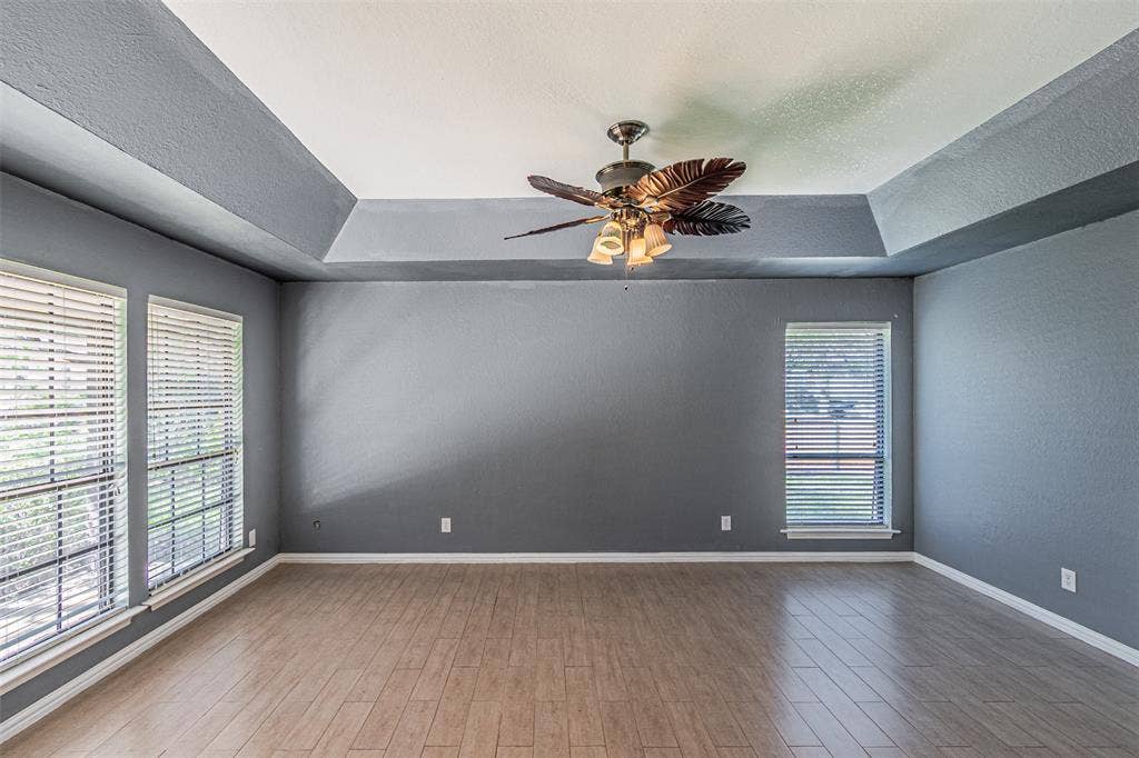 8808 Sylvan Court, Fort Worth, TX 76120 Tray ceiling with a decorative ceiling fan, wood-finish flooring, and multiple windows with blinds