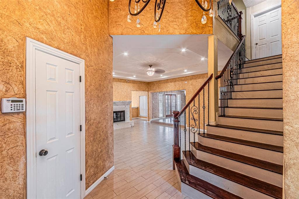 8808 Sylvan Court, Fort Worth, TX 76120 Ornate wrought iron railing, wood-finish stair treads, tile flooring, textured wall finish, and a fireplace with a light-colored surround