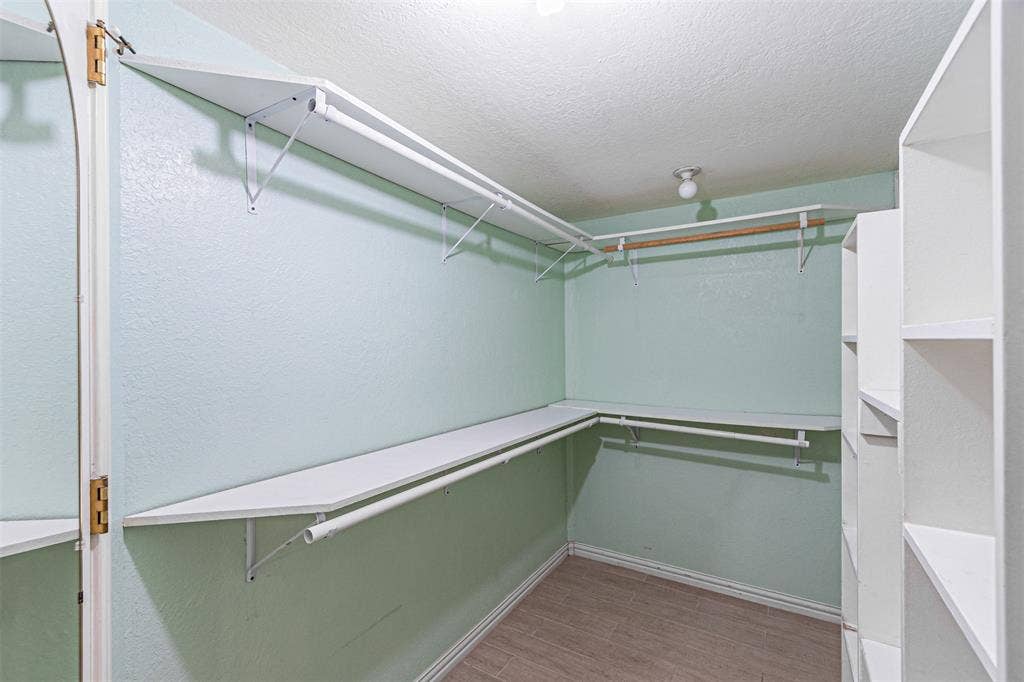 8808 Sylvan Court, Fort Worth, TX 76120 Walk-in closet featuring extensive built-in shelving, multiple hanging rods, and wood-finish flooring