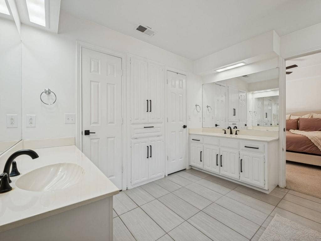 5730 Winding Woods Trail, Dallas, TX 75227 Dual-vanity bathroom featuring white cabinetry with matte black hardware, integrated countertops with undermount sinks, large-scale mirrors, and tile flooring