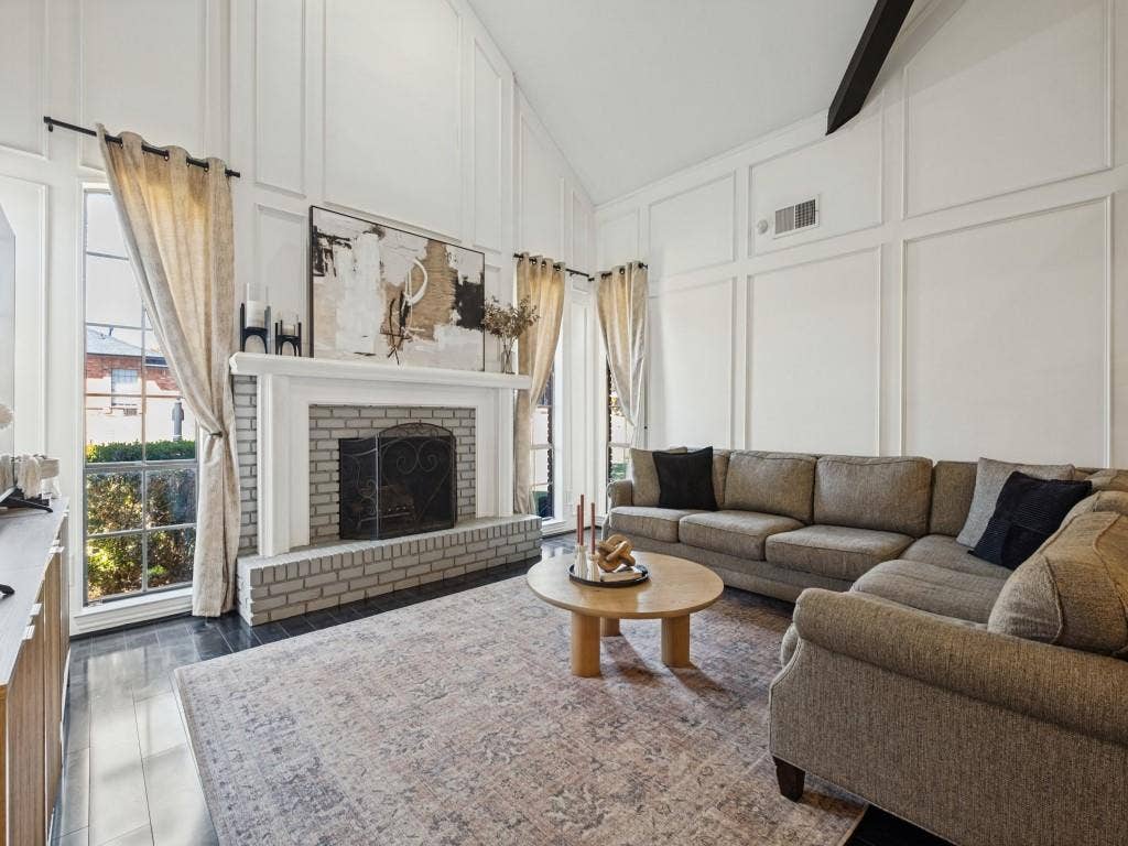5730 Winding Woods Trail, Dallas, TX 75227 Vaulted ceilings with board-and-batten wall detailing, floor-to-ceiling windows, and a brick fireplace featuring a wood mantelpiece and hearth