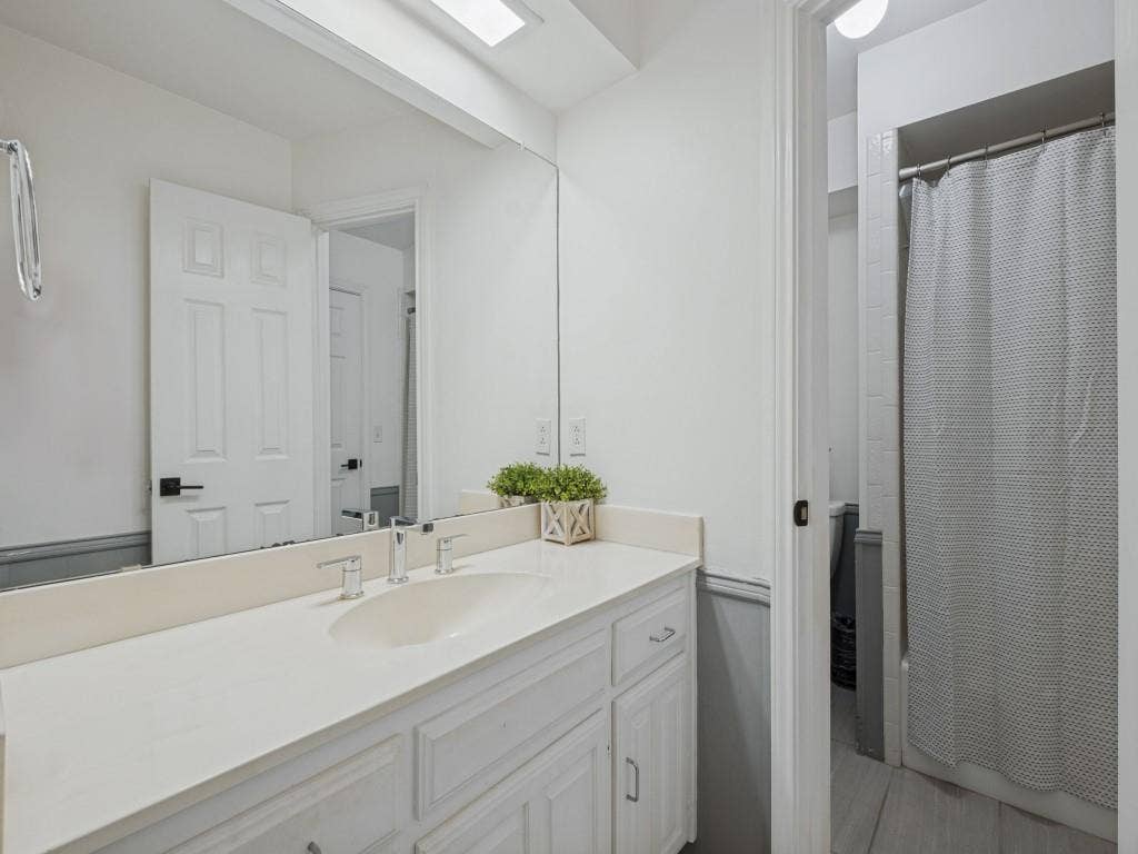 5730 Winding Woods Trail, Dallas, TX 75227 Bathroom vanity featuring a white countertop with an integrated basin, chrome widespread faucet, full-width mirror, and white shaker-style cabinetry
