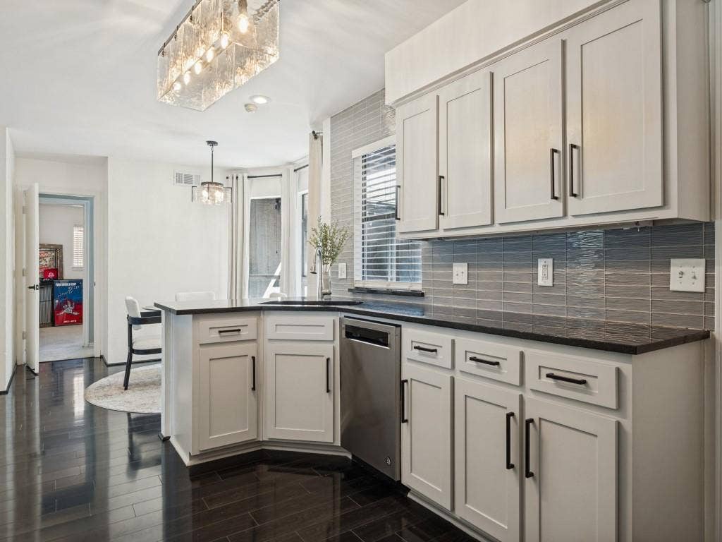 5730 Winding Woods Trail, Dallas, TX 75227 Kitchen featuring white cabinetry with matte black hardware, dark stone countertops, horizontal glass tile backsplash, wood-finish flooring, and a rectangular glass-paneled pendant light fixture