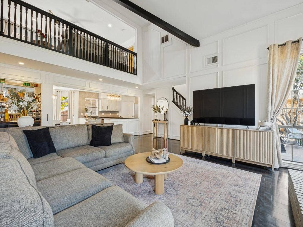 5730 Winding Woods Trail, Dallas, TX 75227 Vaulted ceilings with exposed structural beam, floor-to-ceiling decorative wall paneling, second-level balcony with black railing, and dark hardwood flooring