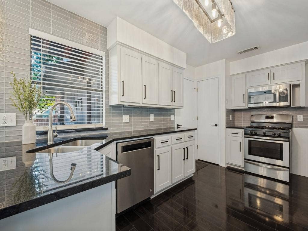 5730 Winding Woods Trail, Dallas, TX 75227 Kitchen featuring white shaker-style cabinetry, dark stone countertops, stainless steel appliances, linear tile backsplash, and wood-finish flooring