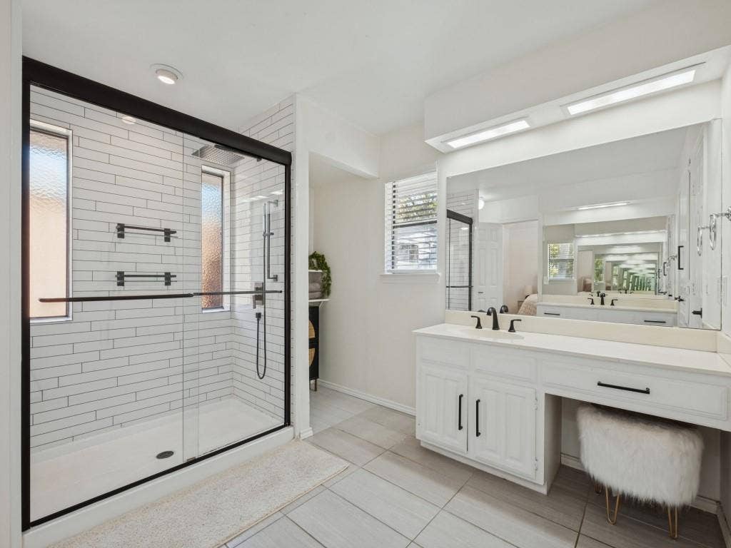 5730 Winding Woods Trail, Dallas, TX 75227 Bathroom featuring a glass-enclosed shower with horizontal wall tile, white cabinetry, dual-faucet vanity with integrated knee space, and large-format tile flooring
