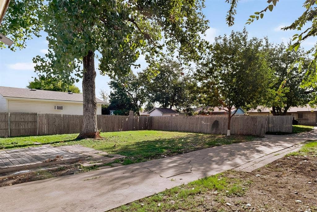 1512 Bay Shore Drive, Garland, TX 75040 Expansive backyard featuring a concrete patio, wood-slat perimeter fencing, and mature trees