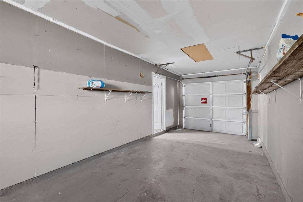 1512 Bay Shore Drive, Garland, TX 75040 Enclosed garage space featuring a paneled sectional door, concrete flooring, built-in wall shelving, and an integrated ceiling access panel