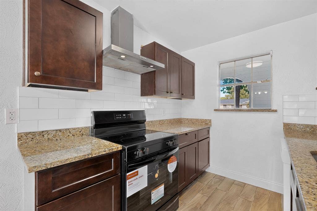 1512 Bay Shore Drive, Garland, TX 75040 Kitchen featuring dark wood cabinetry, stone countertops, white subway tile backsplash, stainless steel range hood, and wood-finish flooring