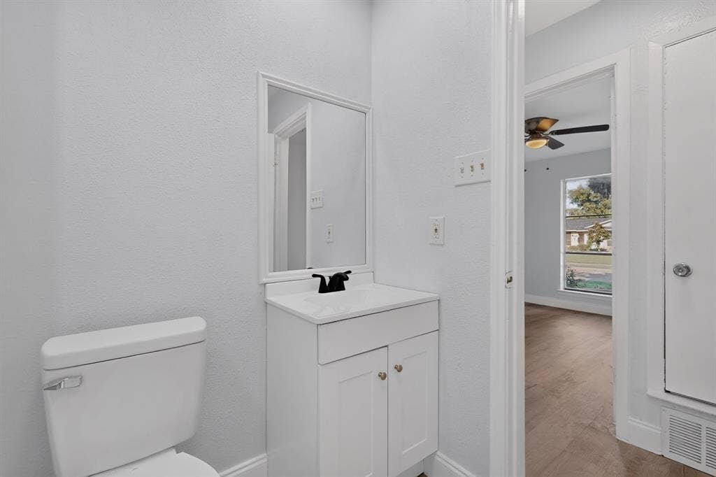 1512 Bay Shore Drive, Garland, TX 75040 White vanity cabinet with a rectangular countertop, framed mirror, matte black faucet, and white toilet