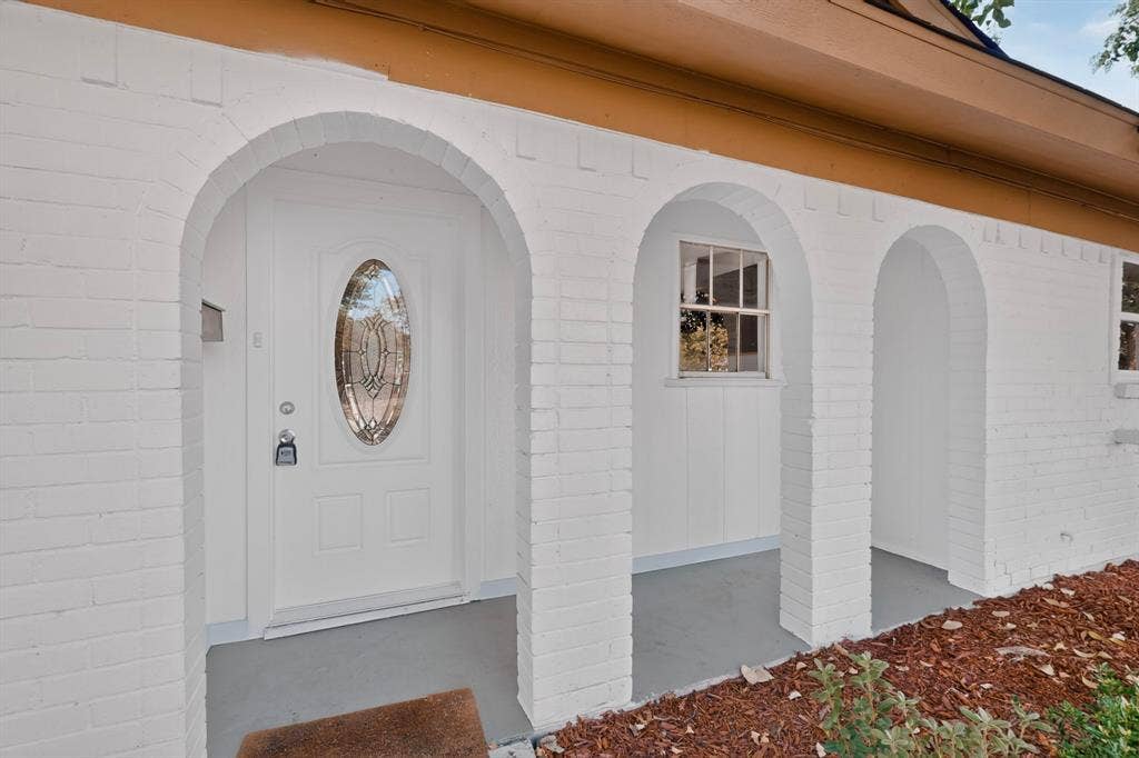 1512 Bay Shore Drive, Garland, TX 75040 Painted brick facade with arched architectural entry, covered porch, and exterior door featuring an oval glass inlay