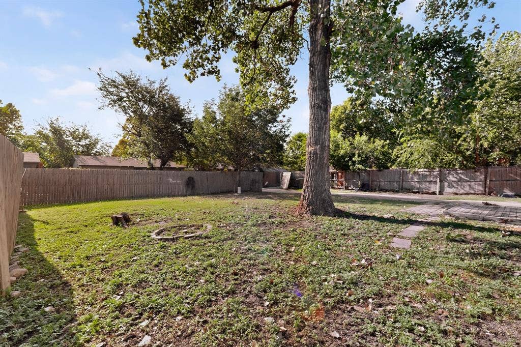 1512 Bay Shore Drive, Garland, TX 75040 Spacious backyard featuring a perimeter wood fence, mature tree, and stone paver area