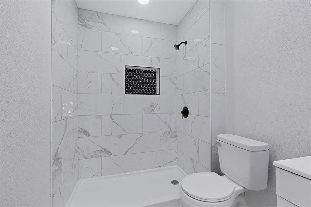 1512 Bay Shore Drive, Garland, TX 75040 Walk-in shower featuring large-format stone-patterned tile, matte black shower fixtures, and a recessed hexagonal tile niche