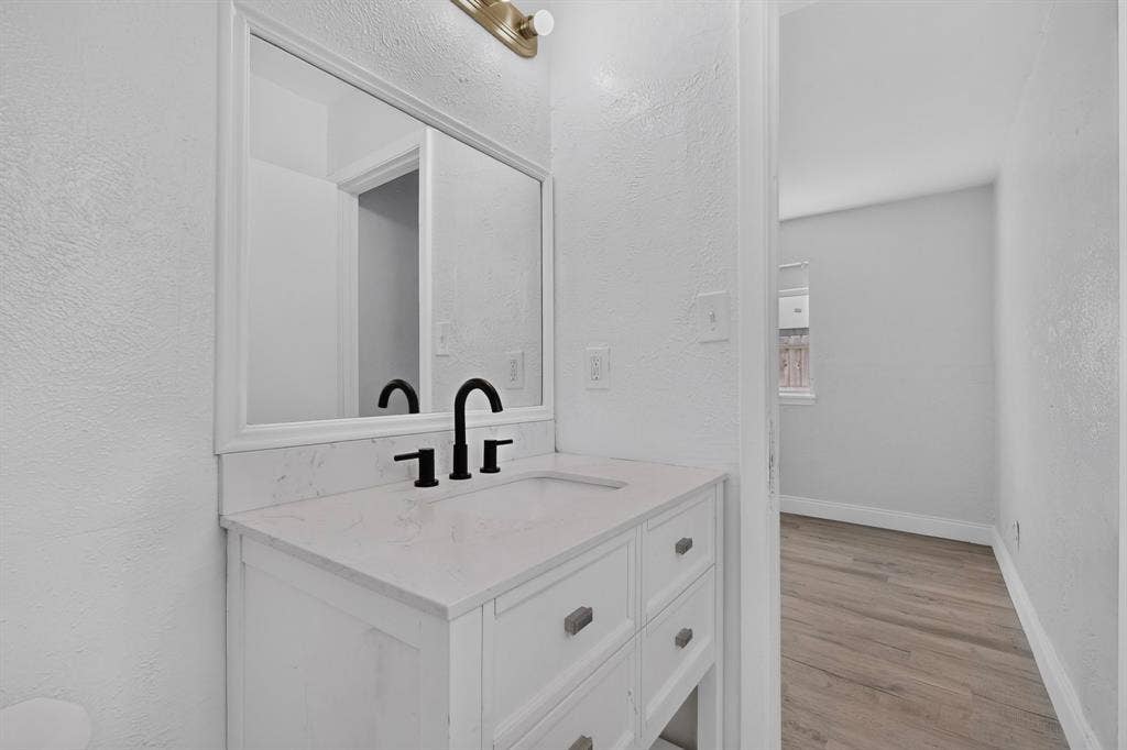 1512 Bay Shore Drive, Garland, TX 75040 White vanity with a stone-finish countertop, integrated basin, matte black faucet, framed mirror, and warm-toned vanity lighting