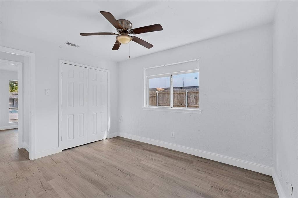 1512 Bay Shore Drive, Garland, TX 75040 Primary bedroom featuring wood-finish flooring, a ceiling fan with integrated lighting, dual-panel closet doors, and a sliding window