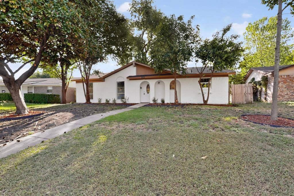 1512 Bay Shore Drive, Garland, TX 75040 Single-story residence featuring a painted brick exterior, arched entryway, concrete walkway, and mature landscaping