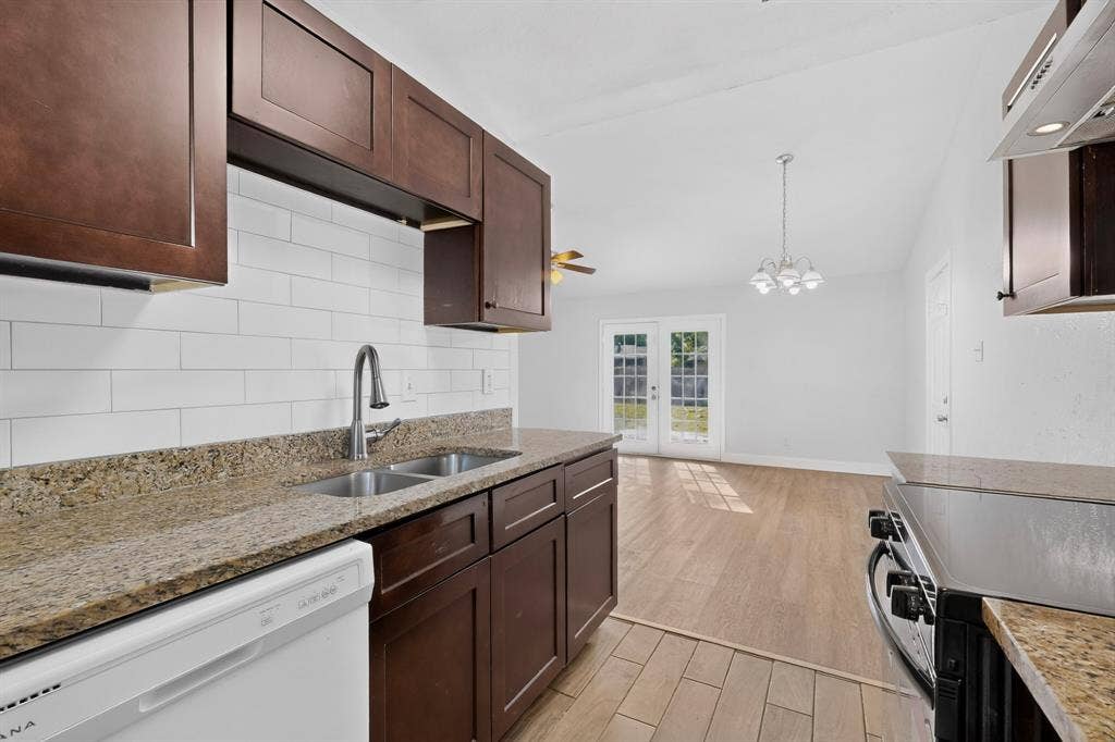 1512 Bay Shore Drive, Garland, TX 75040 Kitchen featuring dark-toned cabinetry, stone-finish countertops, subway tile backsplash, stainless steel faucet, and wood-finish tile flooring