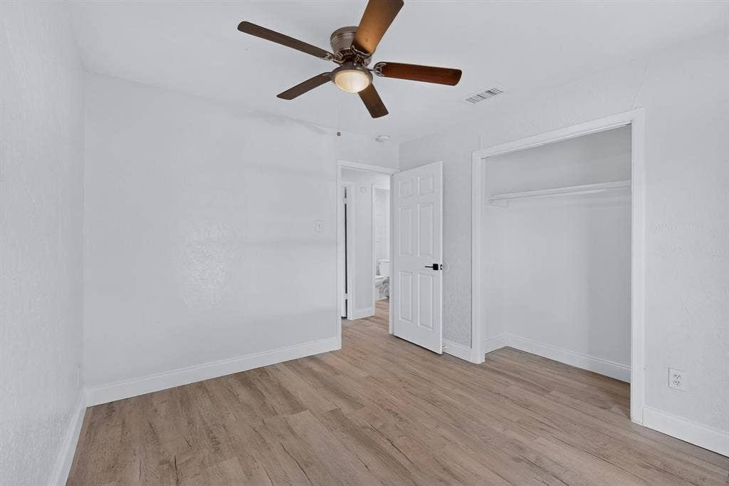 1512 Bay Shore Drive, Garland, TX 75040 Primary bedroom featuring wood-finish flooring, a ceiling fan with integrated lighting, a walk-in closet, and a white six-panel interior door with matte black hardware