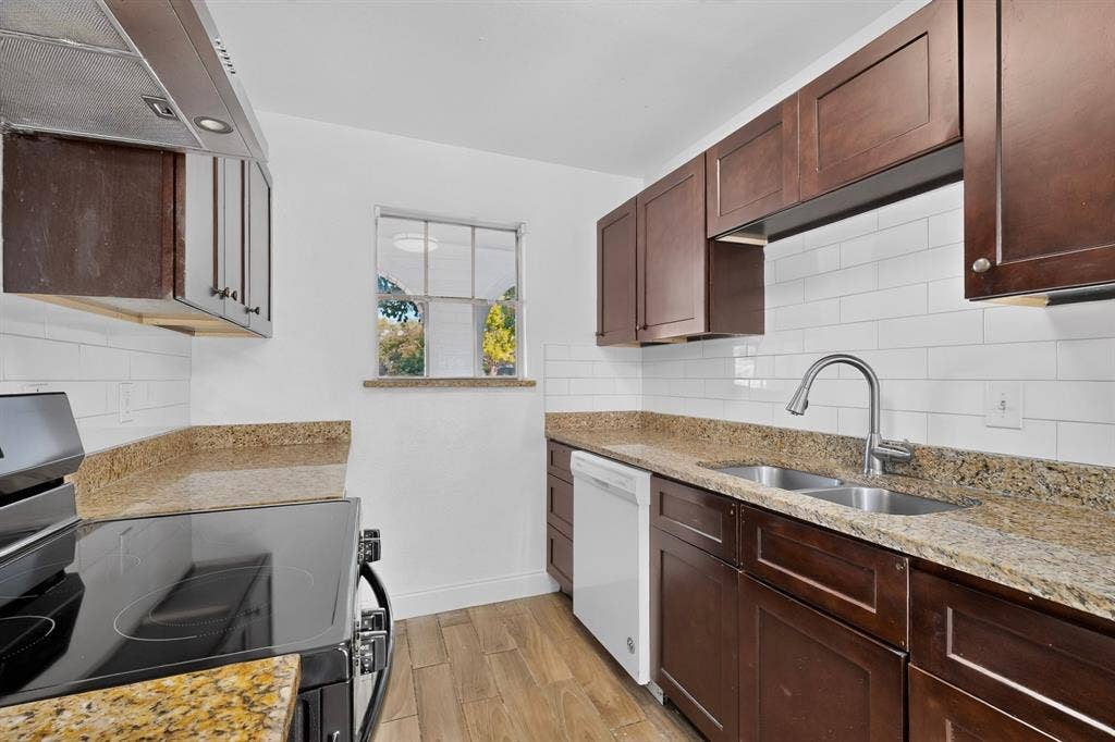 1512 Bay Shore Drive, Garland, TX 75040 Kitchen featuring dark wood-finish cabinetry, stone countertops, white subway tile backsplash, stainless steel dual-basin sink with pull-down faucet, and wood-finish flooring