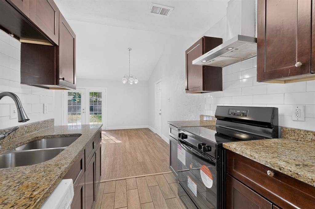 1512 Bay Shore Drive, Garland, TX 75040 Kitchen featuring wood-finish cabinetry, stone countertops, a white subway tile backsplash, stainless steel sink with a high-arch faucet, and wood-finish tile flooring