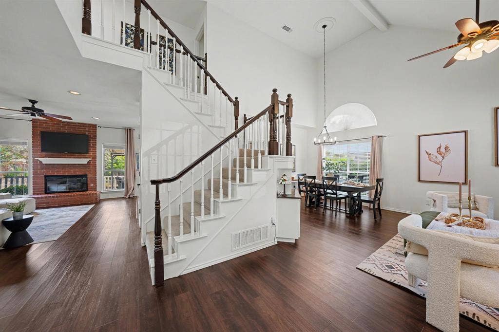 Wood-finish flooring throughout, two-story ceiling, brick fireplace with mantel, and a prominent staircase with white banisters and dark wood railings