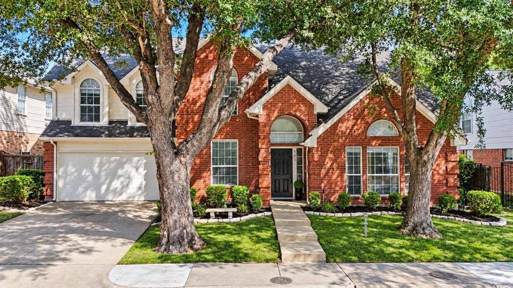 Brick facade with white trim, arched windows, attached two-car garage, and established front landscaping