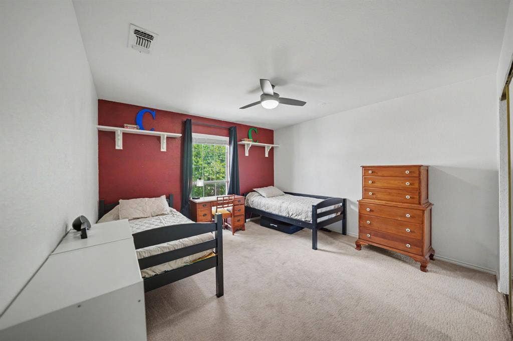 Plush carpet flooring, a ceiling fan with integrated lighting, a window with curtains, and built-in shelving