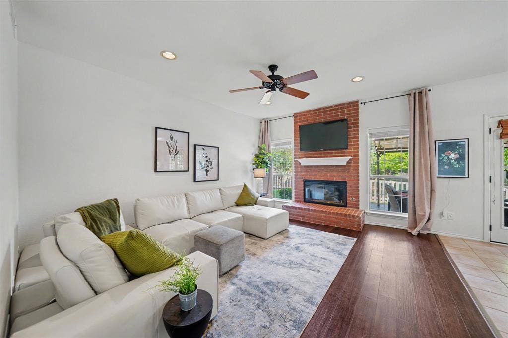 Brick-clad fireplace with a white mantel, ceiling fan with wood-finish blades, recessed lighting, and wood-finish flooring