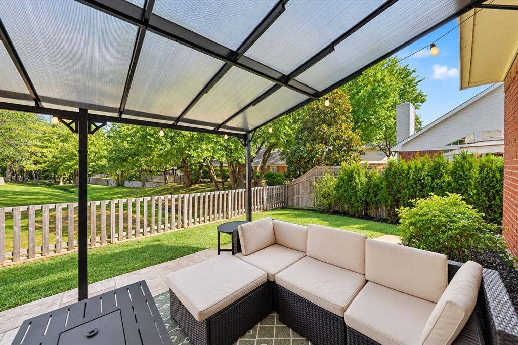 Covered patio with a translucent roof structure, tile flooring, and a fenced backyard with mature trees