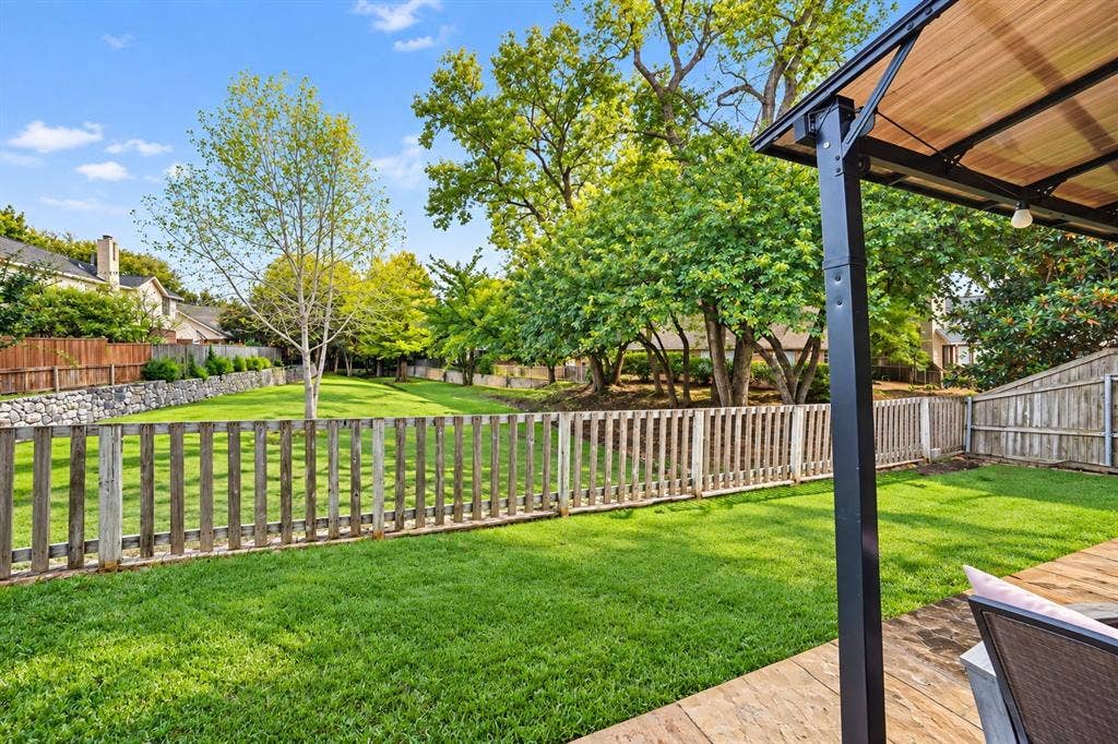 Expansive backyard featuring a manicured lawn, established trees, wood fencing, and a stone retaining wall