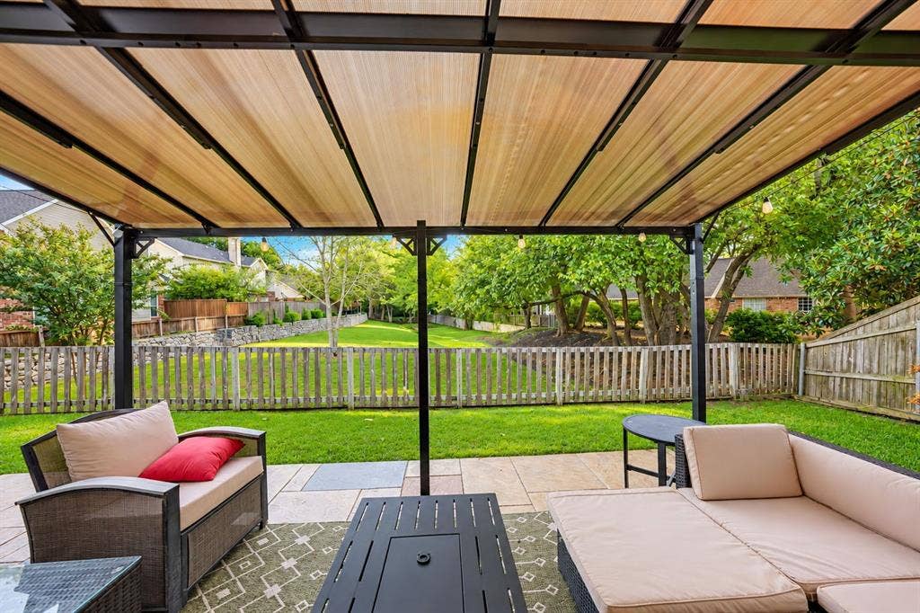 Patio area featuring a structural wood-finish pergola with integrated lighting, concrete paver flooring, and a fenced perimeter