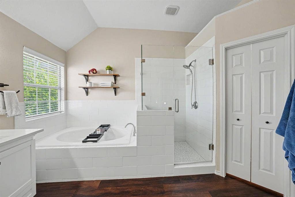 Spacious bathroom featuring a built-in soaking tub, a glass-enclosed shower with white subway tile, and wood-finish flooring