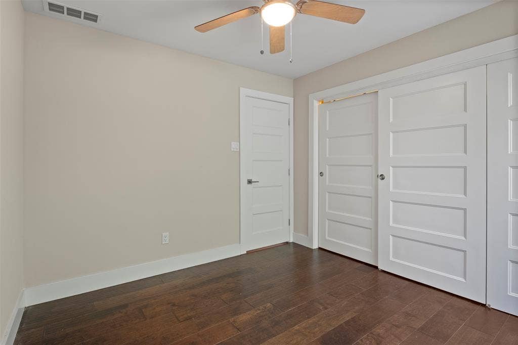Wood-finish flooring with a ceiling fan light fixture, flat-panel interior door, and panel-style sliding closet doors