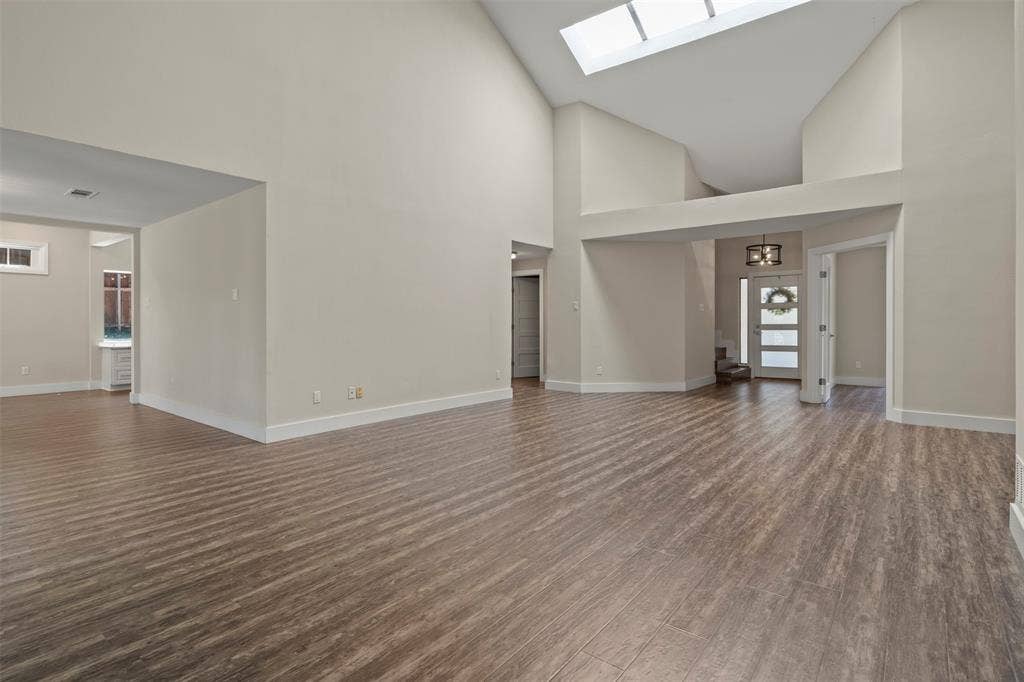 Vaulted ceilings, wood-finish flooring, an overhead skylight, and a white paneled front door with frosted glass inserts