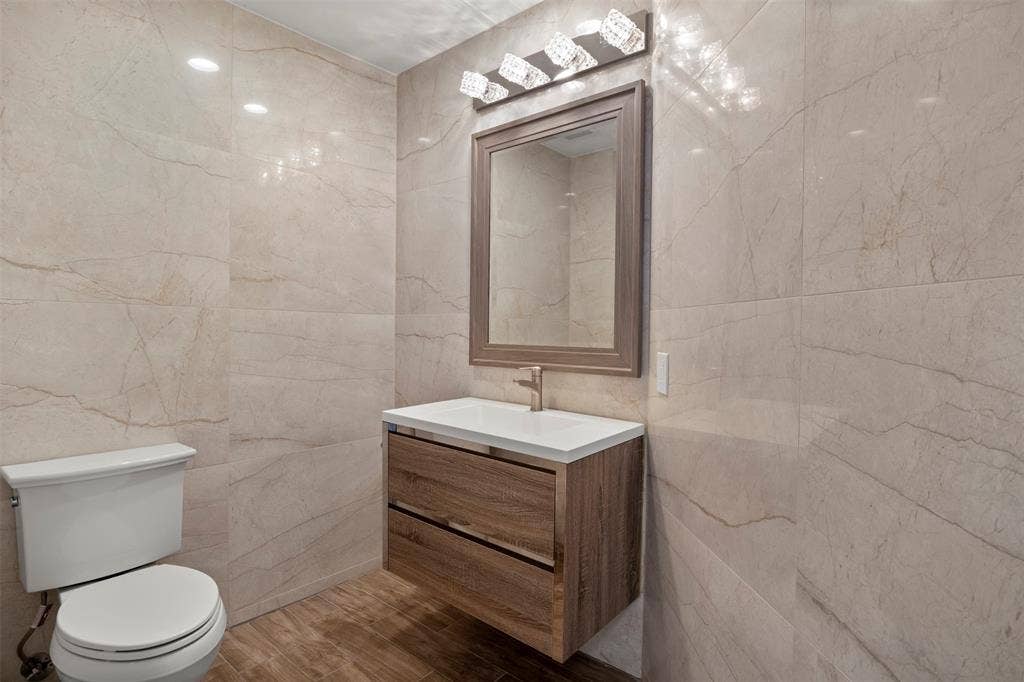 Floating wood-finish vanity with a white countertop and gold-tone faucet, complemented by a framed mirror