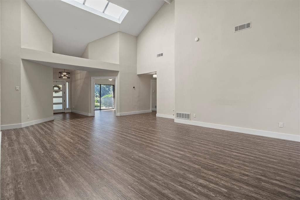 Vaulted ceilings, wood-finish flooring, and a skylight illuminate this expansive living area