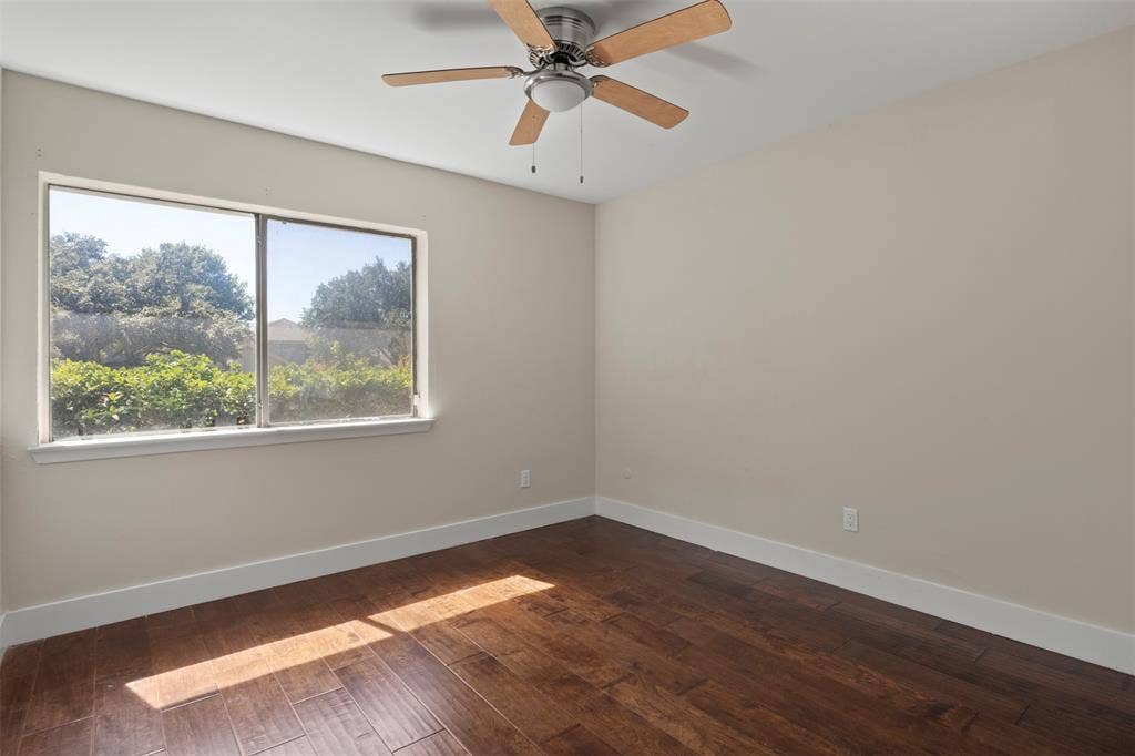 Rich wood-finish flooring, neutral wall tones, and a ceiling fan with light fixture