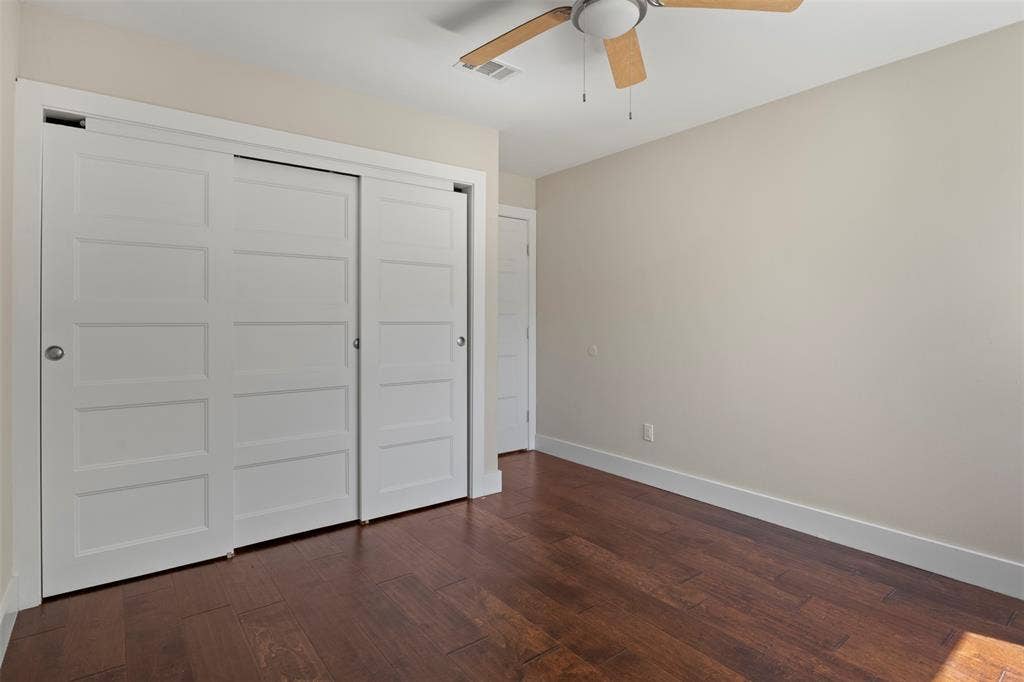 Wood-finish flooring, white sliding closet doors, ceiling fan with light fixture, and light-toned wall paint