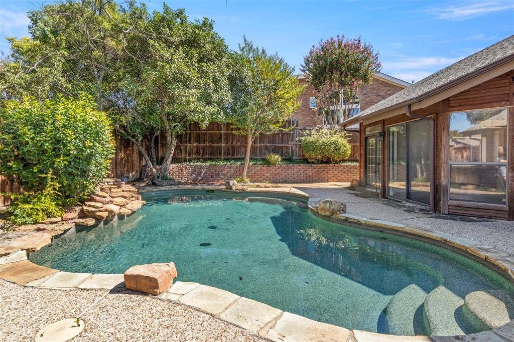 Backyard swimming pool with stone coping, integrated steps, and a rock waterfall feature
