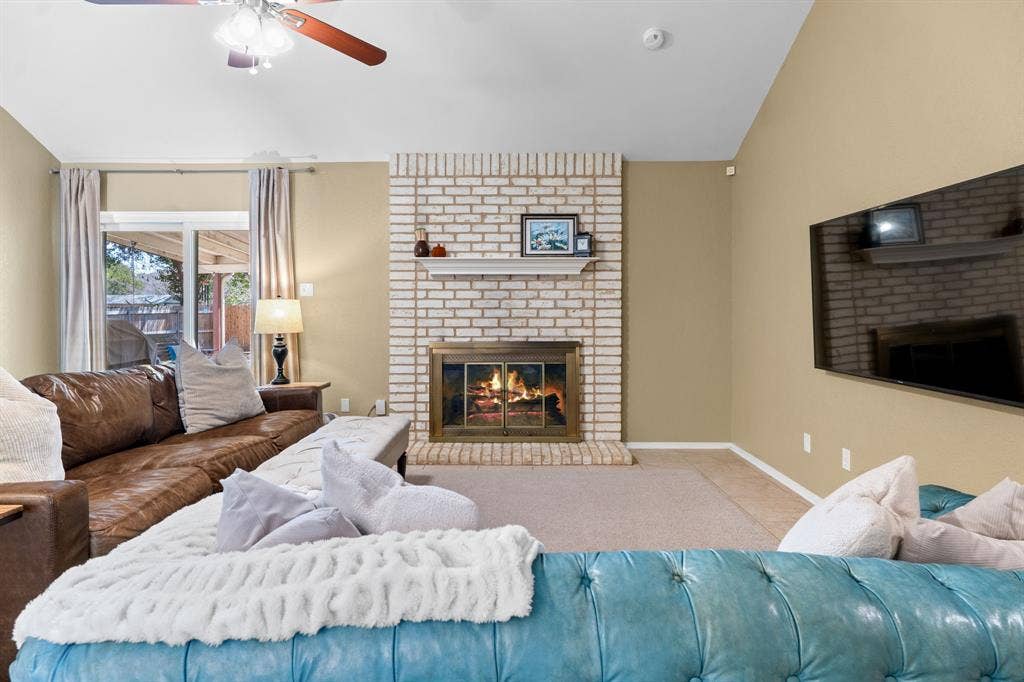 10712 Apache Drive, Waco, TX 76712 Vaulted ceiling, ceiling fan with integrated lighting, brick fireplace with mantel, glass-paneled fireplace insert, and sliding glass door