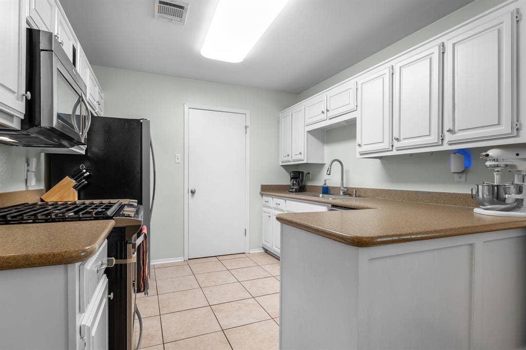 10712 Apache Drive, Waco, TX 76712 White cabinetry with brushed nickel hardware, light-toned countertops, and tile flooring