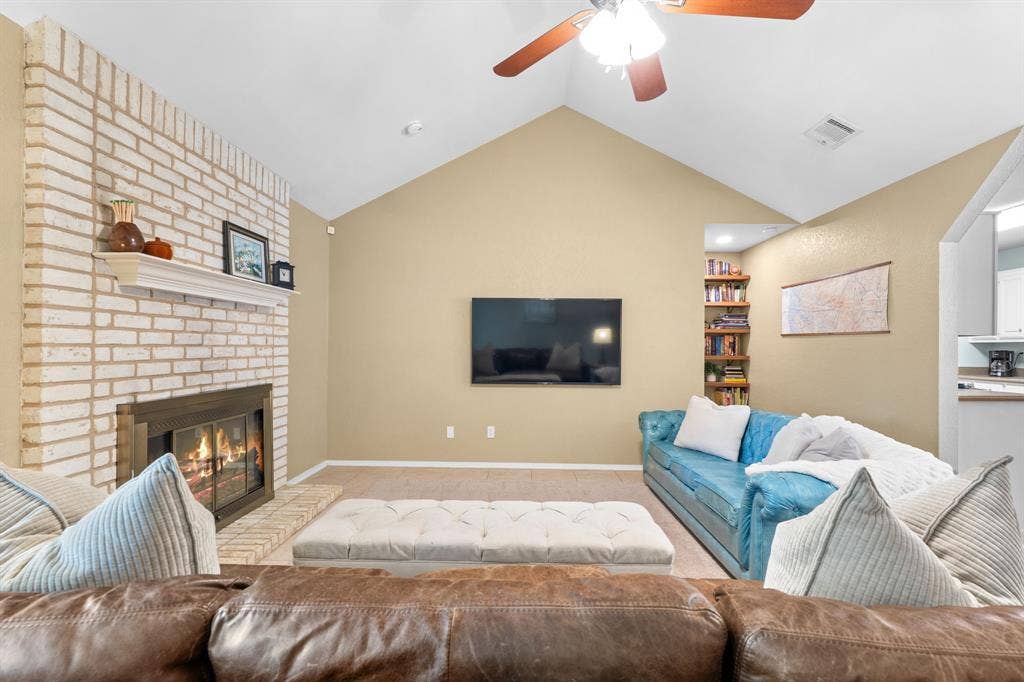 10712 Apache Drive, Waco, TX 76712 Vaulted ceiling with a ceiling fan, white brick fireplace with a mantel, built-in shelving, and carpeting